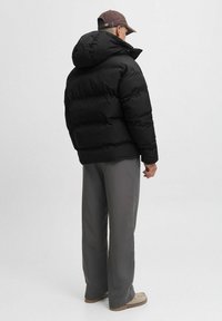 Giacca a pompa nera con un cappuccio ampio e design trapuntato. Abbinata a pantaloni grigi a vestibilità ampia e calzature chiare.
