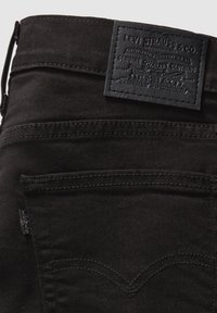 Vaqueros de mezclilla negra con una superficie texturizada, con un parche de cuero negro y costuras tonales. Incluye bolsillos traseros con costuras curvas.