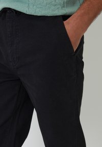 Pantalones de algodón negros con corte recto, que cuentan con bolsillos laterales y una textura suave. La cinturilla es ajustable para mayor comodidad.