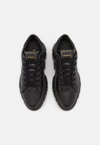 Czarne skórzane sneakersy z zaokrąglonym noskiem, teksturowaną powierzchnią, płaskimi sznurówkami i złotym akcentem logo na języku. Wyposażone w wyściełaną podeszwę i smukły design.