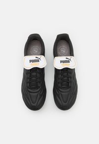 Zapatos de fútbol negros con una parte superior texturizada, que cuentan con una correa blanca y un logo etiquetado como "PUMA KING". Diseño con cordones y con interior acolchado.