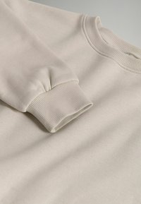 Šviesiai smėlinis megztinis su gipiūro apykakle ir rankovėmis, pasižymintis minkšta tekstūra ir laisva siluetu. Lygus audinys be matomų raštų.