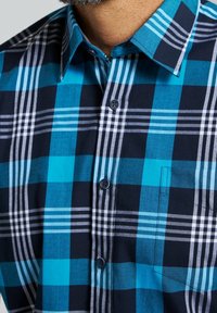 Rutigt skjorta med knappar i blå och marinblå färgskala med vita och grå accenter. Tillverkad av bomull, med standardkrage och ficka.