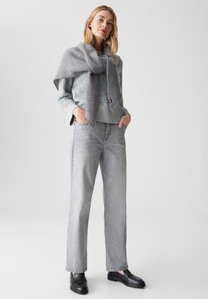 Maglione grigio in lana con una finitura strutturata, abbinato a jeans dritti grigio chiaro. Mocassini neri completano l'outfit. Toni morbidi e smorzati.