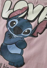 Różowy materiał przedstawia postać z kreskówki o niebieskiej skórze i czarnych akcentach, ozdobioną świecącym różowym detalem uszu z cekinów.