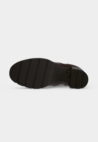Semelle d'une chaussure marron foncé avec une semelle extérieure en caoutchouc rainurée et un talon bloc présentant des rainures horizontales.