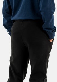 Pantalones negros con una textura suave, bolsillos a cada lado, combinados con una camisa de manga larga azul oscura. Enfoque en el diseño ajustado.