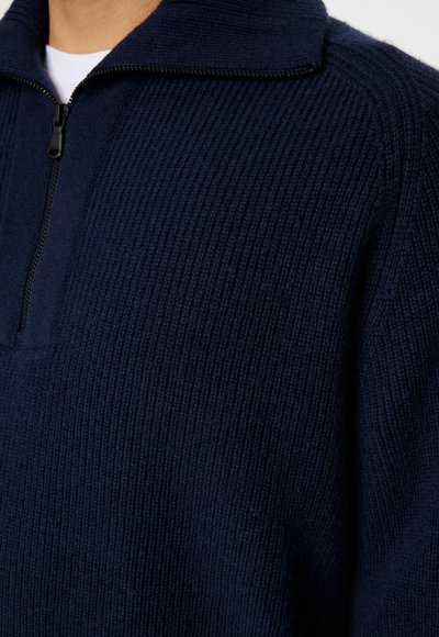 Mörkblå halvdragkedja tröja i ribbad textur, med hög krage och svart dragkedja. Mjukt stickat material med en ren, minimalistisk design.