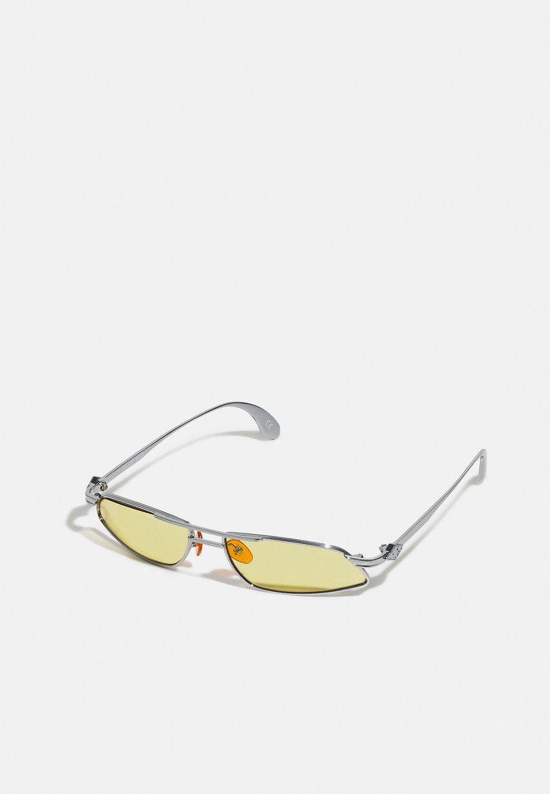 Sunglasses with metallic silver frame, yellow tinted lenses, and orange accents. Aero-dynamic shape with sleek, minimal design.