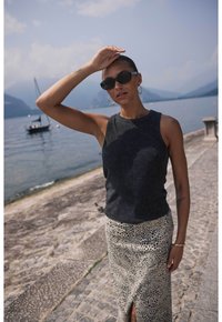 Top sans manches noir avec un col rond, associé à une jupe à motif léopard de couleur claire avec une fente sur le côté. Lunettes de soleil et boucles d'oreilles créoles.