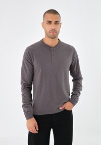 Langärmliges, dunkelgraues Henley-Shirt mit glatter Textur, Drei-Knopf-Blende und Raglanärmeln, kombiniert mit schwarzen Hosen.