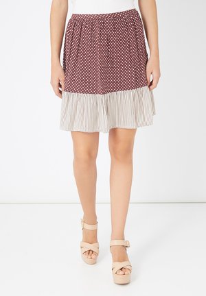 Mujer vistiendo una falda a la altura de la rodilla con lunares marrón y un dobladillo de volantes a rayas beige, combinada con sandalias de plataforma beige.