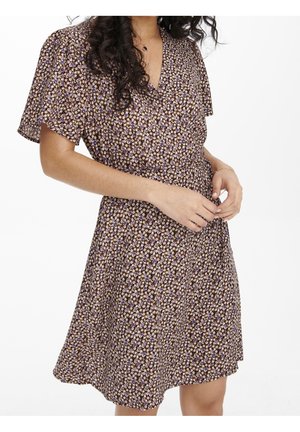 Woman wearing a purple and beige floral wrap dress with flutter sleeves, adjusting the waist tie, against a white background.