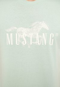 Light green cotton T-shirt featuring a white graphic of a galloping horse and the word "MUSTANG" in bold letters.