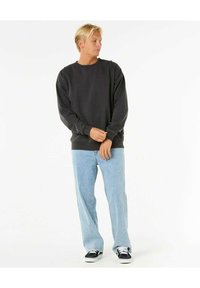 Sudadera gris oscuro con cuello redondo, corte relajado y mangas largas, combinada con jeans de color azul claro y zapatillas negras.