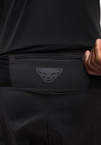 Κοντινό πλάνο ενός ατόμου που φοράει μαύρη αθλητική ενδυμασία με μαύρο τσαντάκι μέσης με φερμουάρ, που φέρει διακριτικό λογότυπο ζώου στο πίσω μέρος.