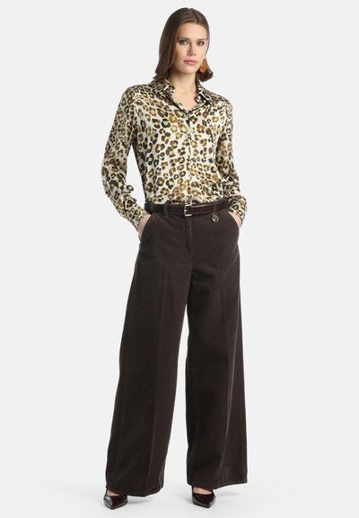 Blusa in seta con stampa leopardata abbinata a pantaloni larghi in corduroy marrone. L'outfit presenta una vita con cintura e un accento argento, insieme a scarpe a punta.