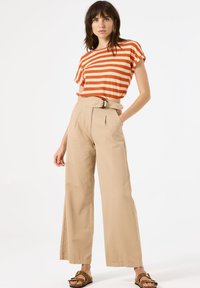 Gestreepte oranje en witte top met korte mouwen, gecombineerd met beige hoge taille wijde broek met een riem en plooien, en bruin sandalen.