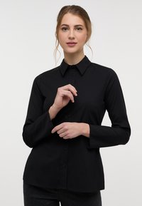 Black long-sleeve button-up shirt with a pointed collar, featuring a smooth texture and a tailored fit, designed for a modern look.