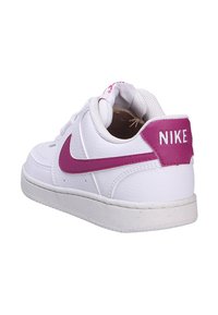 Białe skórzane sneakersy Nike z różowym logo Swoosh i tylna częścią. Posiadają teksturowaną powierzchnię oraz sznurowany przód z otworami dla lepszej wentylacji.