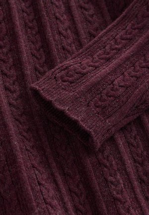 Burgundy cable-knit wool sweater sleeve folded over matching sweater body, showing textured knit pattern and ribbed cuff.