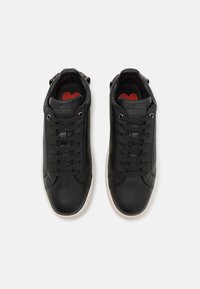 Zwarte leren sneakers met platte veters, logo op de tong en een rood hartaccent op de binnenzool; witte rubberen zool. Klassiek laag ontwerp.