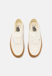 Baskets en toile blanches avec bout rond, design lacé et semelle en caoutchouc beige. Présente un logo sur la languette et une étiquette latérale. Texture lisse partout.