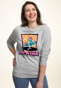 Felpa grigia con polsini a coste, caratterizzata da un design grafico colorato di uno skateboarder, con il testo "Sii gentile, la vita è breve" in caratteri in grassetto.
