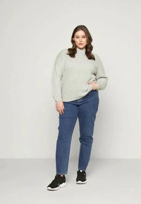 Pulôver de malha cinza claro com gola alta, combinado com jeans azul médio e ténis pretos. O pulôver tem um corte descontraído e detalhes canelados.