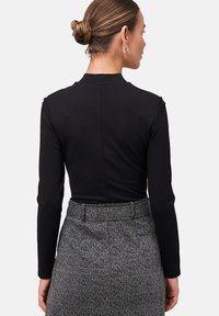 Top noir à manches longues avec un col haut et une texture lisse, associé à une jupe à motifs avec un design gris et noir.