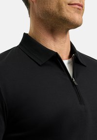 Zwarte poloshirt met een ritskraag; heeft een effen textuur en een slanke kraagontwerp, wat een moderne uitstraling benadrukt.