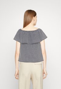 Top décolleté avec un motif vichy noir et blanc, présentant un design à volants en double couche et une coupe décontractée.