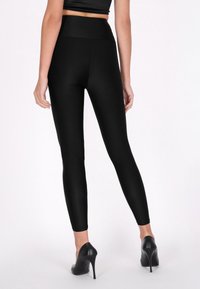 Fekete, magas derekú leggings sima, rugalmas anyagból, testhezálló fazonban, teljes hosszúságú szabásban, fekete magassarkú cipővel párosítva.