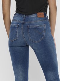 Jeans de denim en azul oscuro con una textura suave, que presentan bolsillos traseros, detalles de costura y una etiqueta de cuero marrón en la cinturilla trasera.