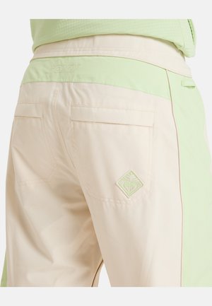 Beige trousers with a light green waistband, featuring two back pockets and a diamond-shaped embroidered logo on the right pocket.