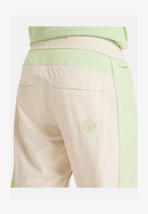 Beige trousers with a light green waistband, featuring two back pockets and a diamond-shaped embroidered logo on the right pocket.