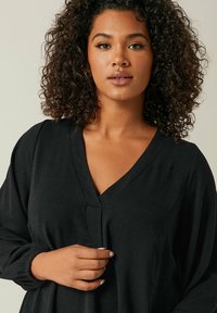 Schwarze Langarmbluse mit V-Ausschnitt und elastischen Bündchen, aus einem glatten, strukturierten Stoff und in lässiger Passform.
