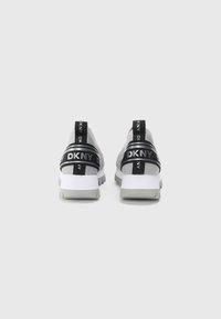 Szare buty sportowe z czarnymi paskami z logo "DKNY", biała podeszwa i teksturowana górna część. Gruby, sportowy design.