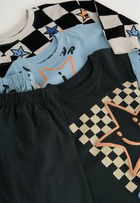 Drie kleurrijke t-shirts gestapeld: één zwart-wit geblokt, één lichtblauw met een sterdesign, en één donker met een ster- en blokkenschema.