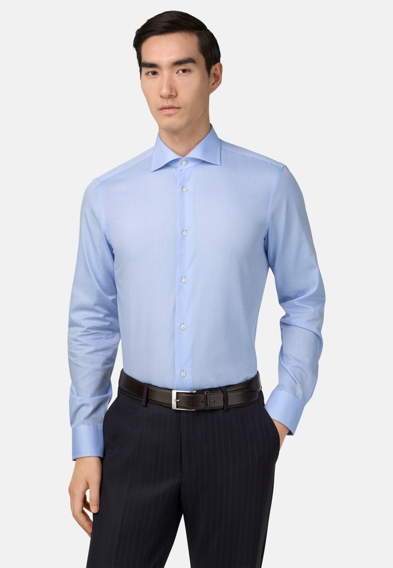 Heledasinine pikkade varrukatega särk terava kraega, diskreetsete vertikaalsete triipudega ja nööbiga, täiustatud tumepruuni vööd ja triibuliste pükstega.