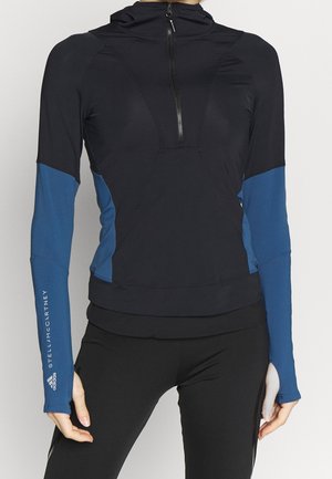 Gros plan d'une personne portant un haut de sport à manches longues noir et bleu avec une fermeture éclair frontale et des trous pour les pouces sur les manches.