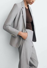 Šedý oblek na mieru s jednoradovým sakom a klopovými revermi a úzkymi nohavicami. Hladká tkanina s jemnou textúrou.