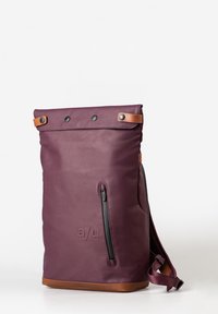 Zaino impermeabile viola con dettagli in pelle marrone, chiusura a rotolo, tasca laterale con zip e logo in rilievo sulla parte anteriore.
