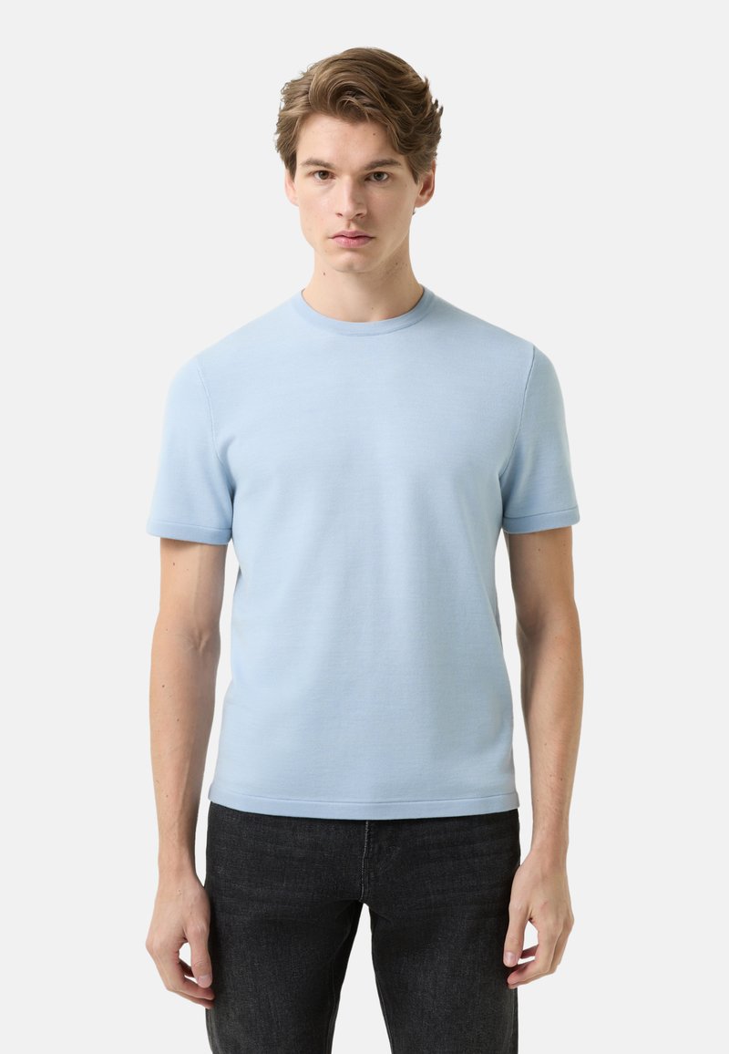 Light blue cotton t-shirt with short sleeves, crew neckline, and a smooth texture, paired with dark jeans. No patterns or noticeable accents.