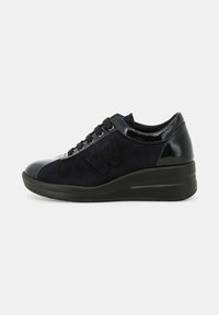 Scarpa sportiva nera con tomaia in suede, accenti lucidi e suola a zeppa. Presenti lacci e un dettaglio logo testurizzato.