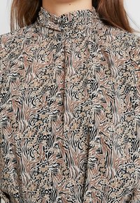 Blusa multicolor con cuello simulado, con un patrón ondulado en tonos de negro, marrón y beige sobre un fondo claro.