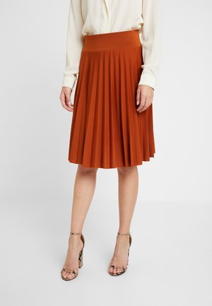 Falda midi plisada color óxido con una cinturilla ancha, hecha de tela suave; combinada con tacones altos de tiras con estampado animal.