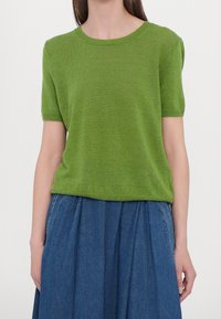 Top verde a maniche corte in maglia con scollo rotondo, abbinato a una gonna in denim blu plissettata. Tessuto morbido e vestibilità rilassata.