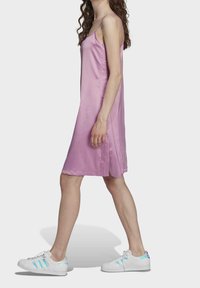 Różowa satynowa sukienka na ramiączkach, o długości midi, z gładką fakturą i detalami w bocznych szwach. Noszona z białymi trampkami.