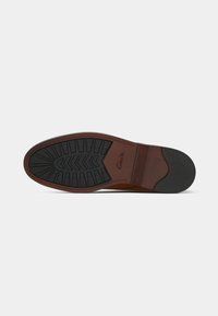Zool van een bruine nette schoen met zwarte rubberen loopvlak en hak, met het merknnaam "Clarks" in reliëf bij de voetboog.